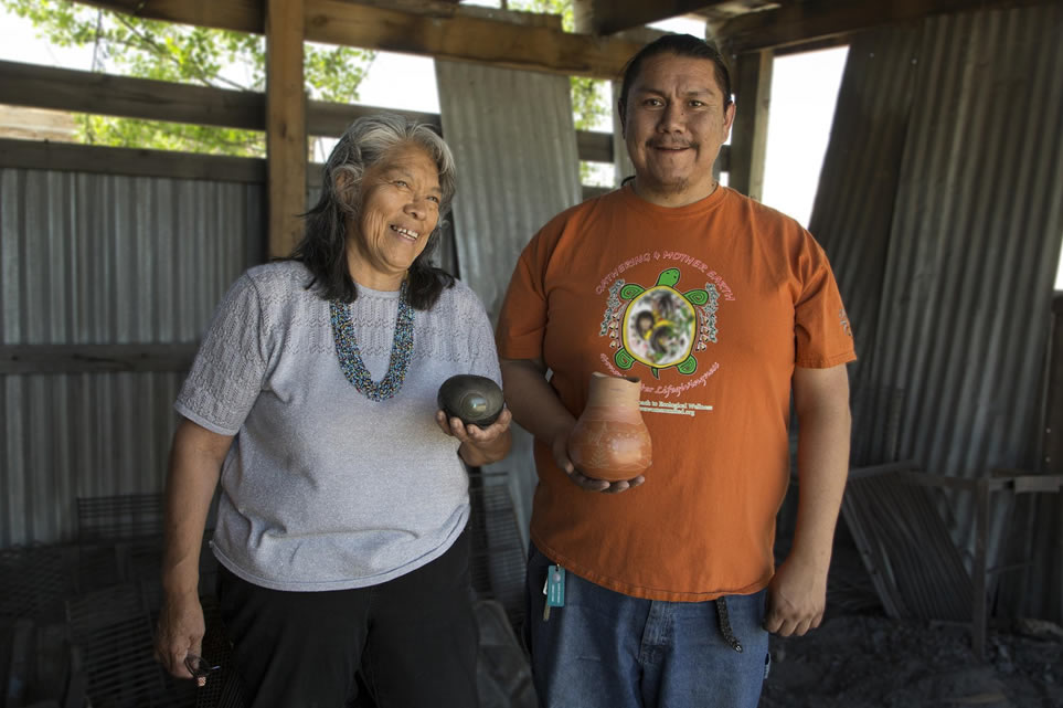 Kathy Wan Povi Sanchez and Wayland Sanchez stand in a an outdoor structure holding their pottery.